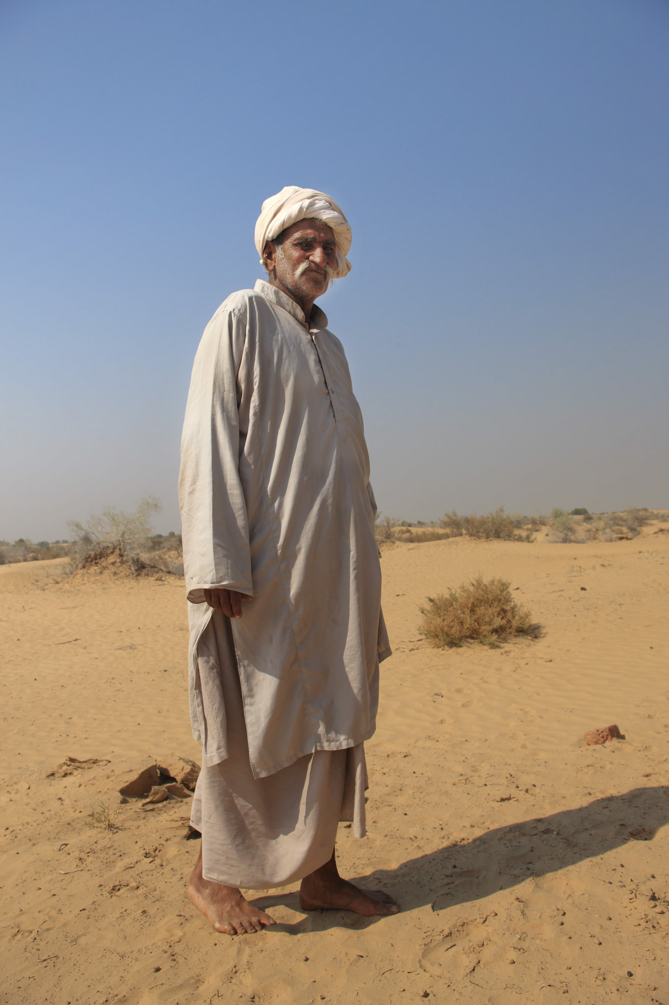 A elder gentleman stands in the desert and waits for his company.