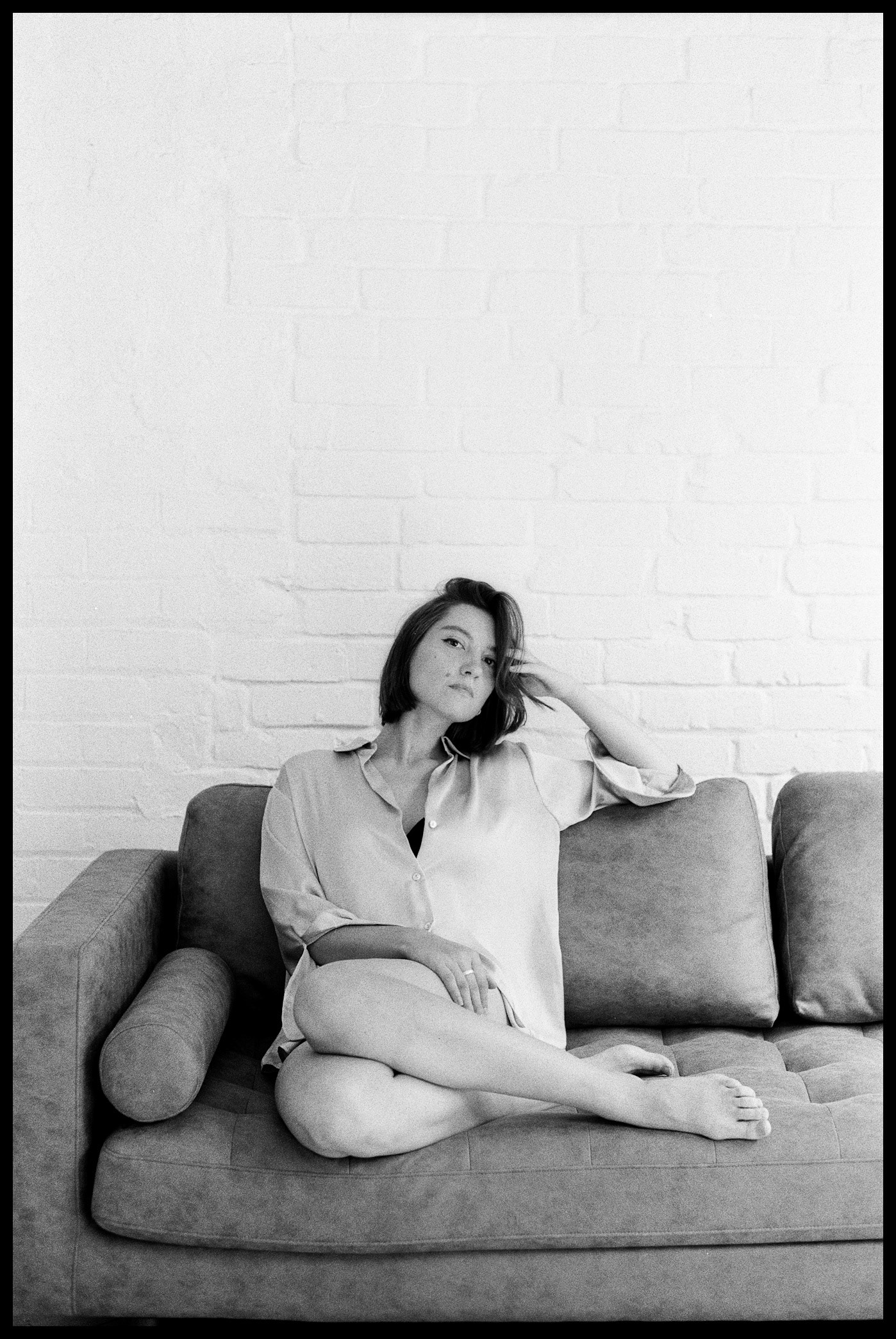 image of a beautiful woman reclining on a couch, looking seductively at the camera, wearing a shirt and with bare legs, crossed.