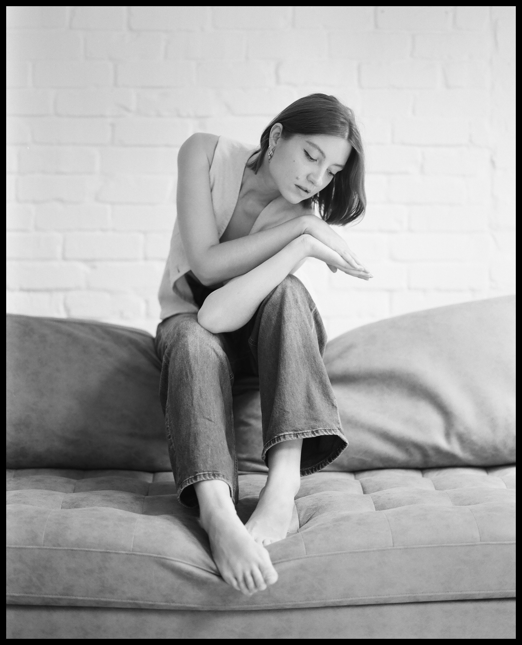image of a beautiful woman sitting on the back of a sofa, with her hands clasped together, bare feet and deep in her own thoughts
