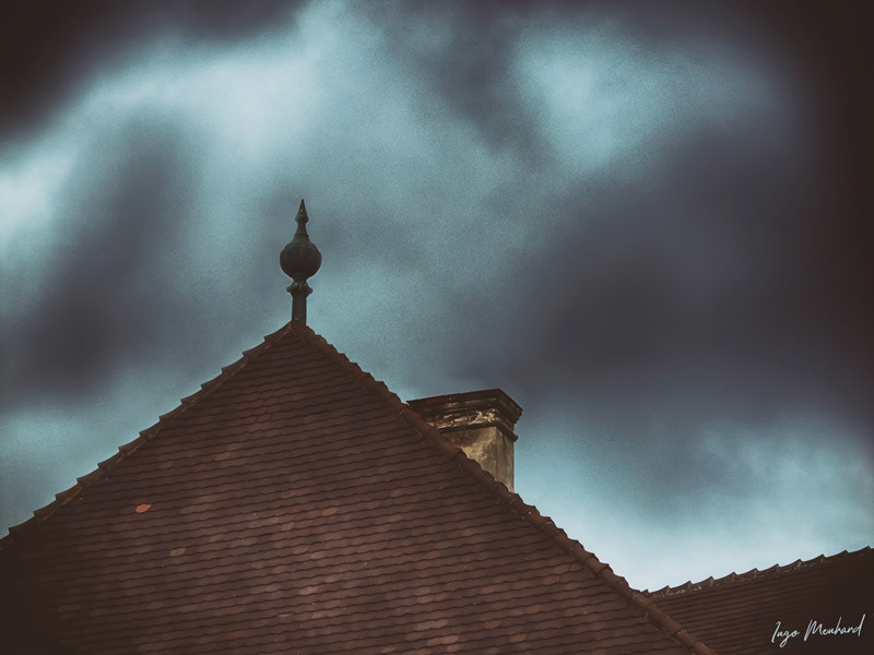 A dark sky behind the peak of an old historical rooftop. The chimney in the back is old and derelict.                               