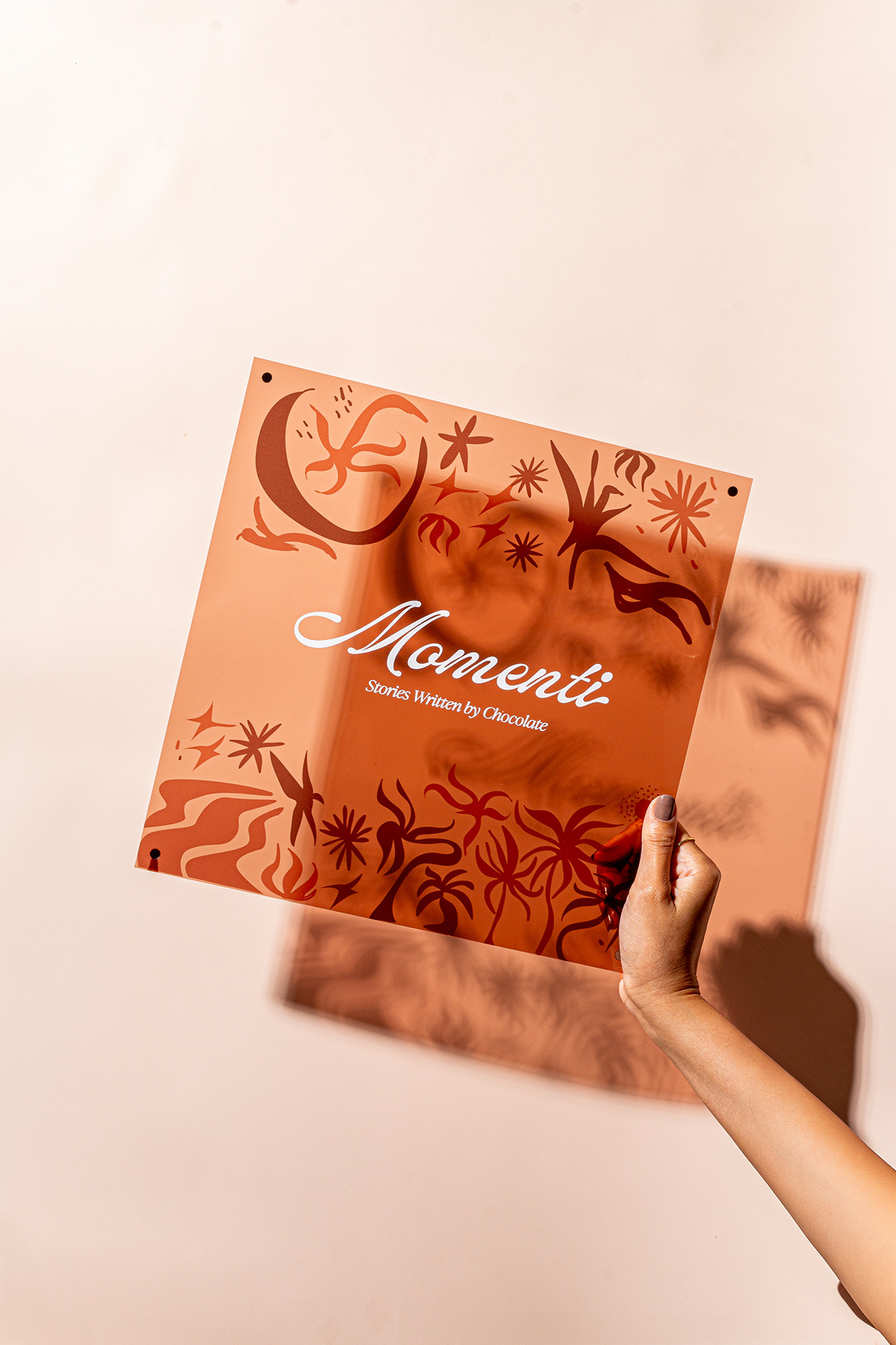 Hand holding an illustrated Momenti menu against a sunlit cream wall