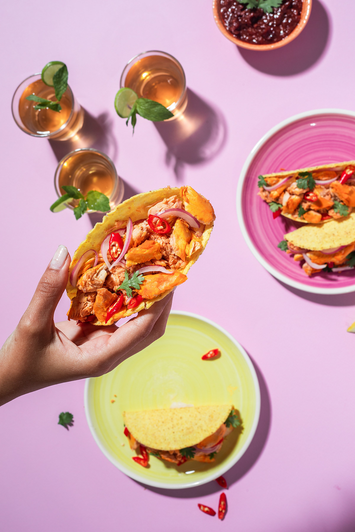 Hand lifting a sandwich above a pink table set with plates and drinks