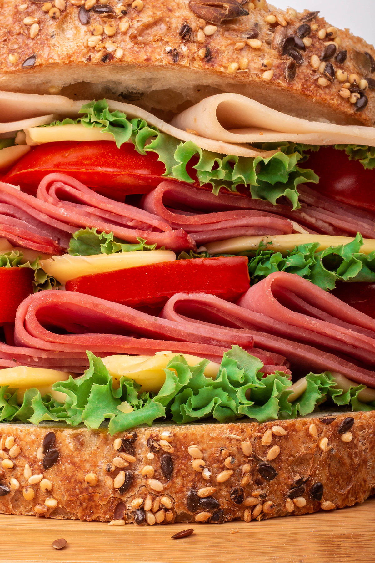 Close crop of a layered deli sandwich with meat, cheese, lettuce and tomato