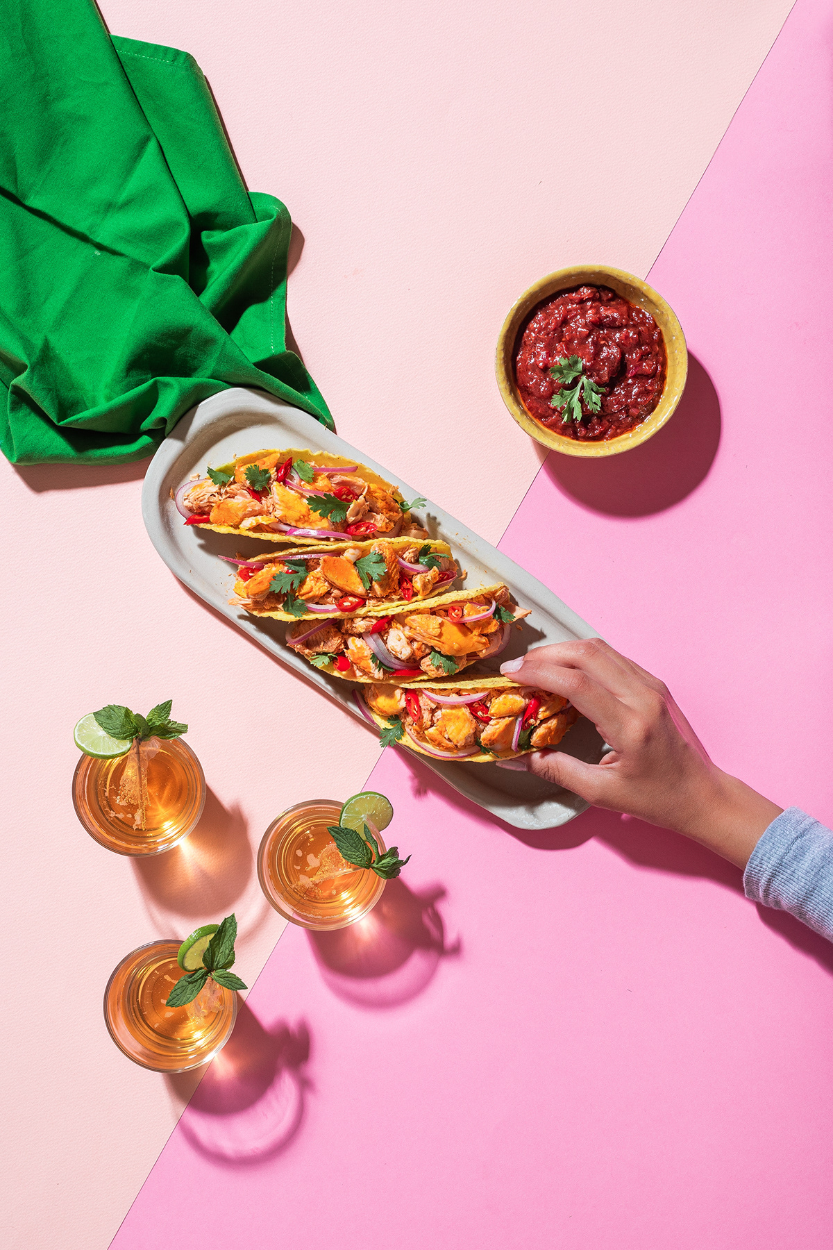 Hands serving a long open sandwich across a pink and green table setting