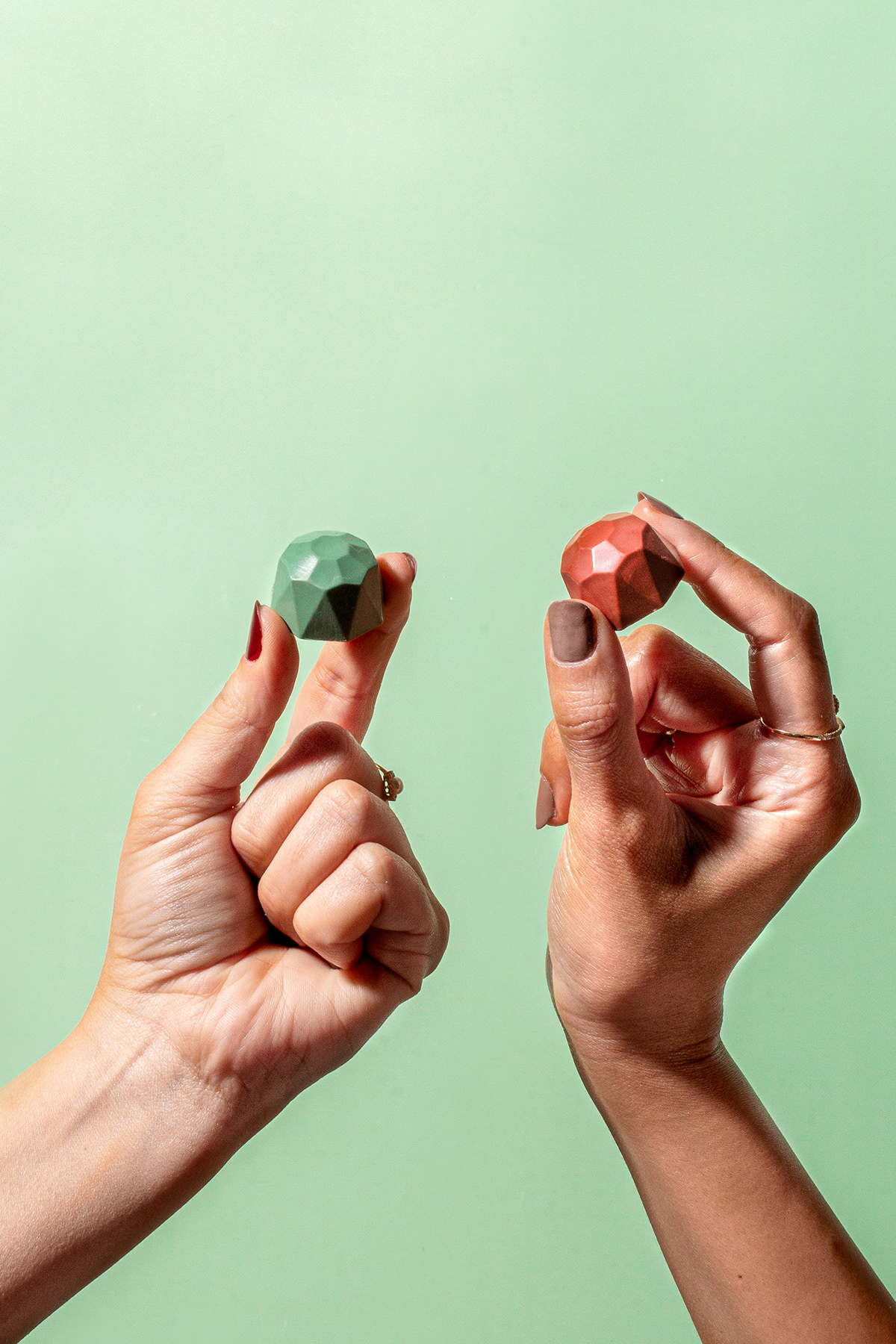 Two hands holding colorful chocolate pieces against a mint-green background