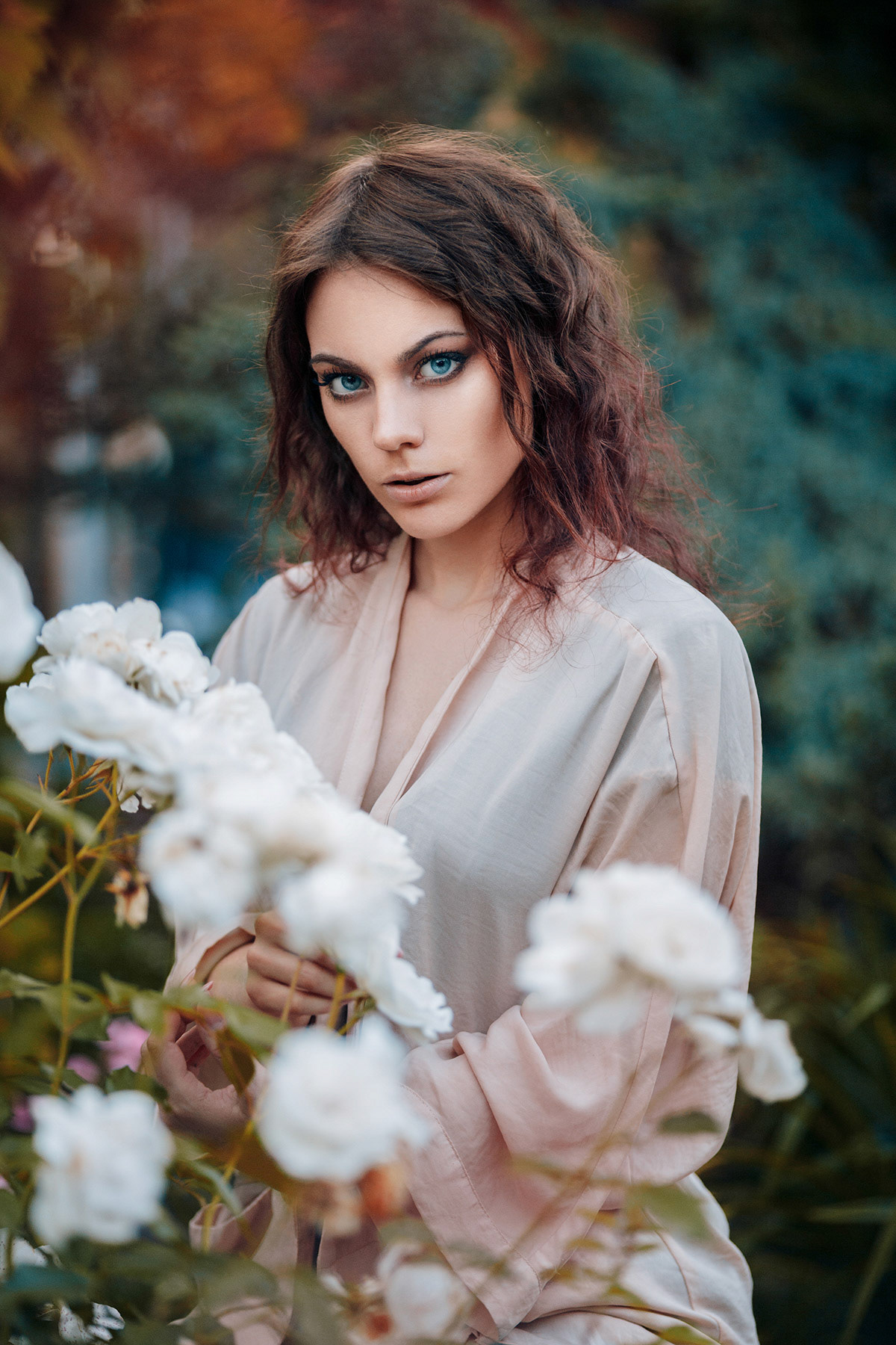 Beautiful young woman with curly hair near roses in a garden. Perfectly retouched.