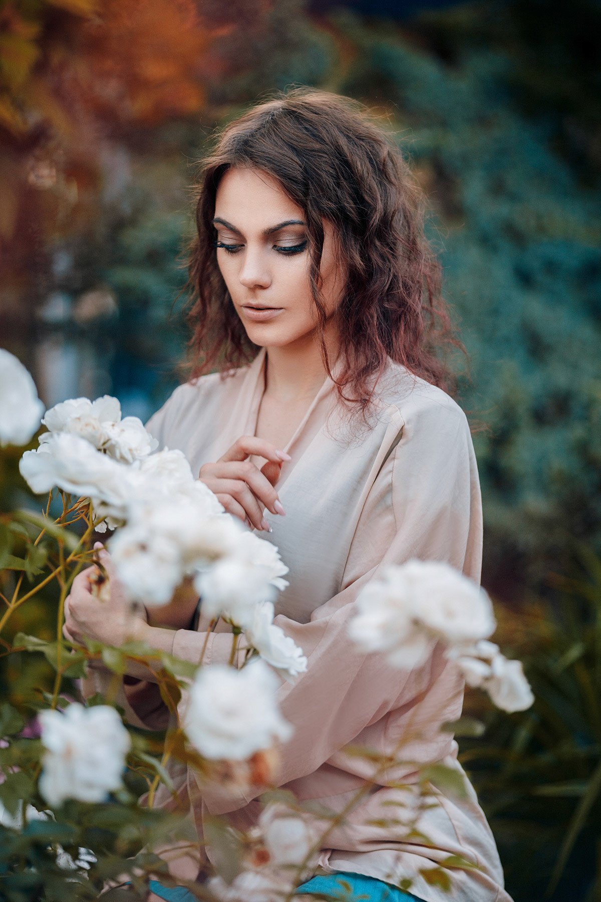 Beautiful young woman with curly hair near roses in a garden. Perfectly retouched.