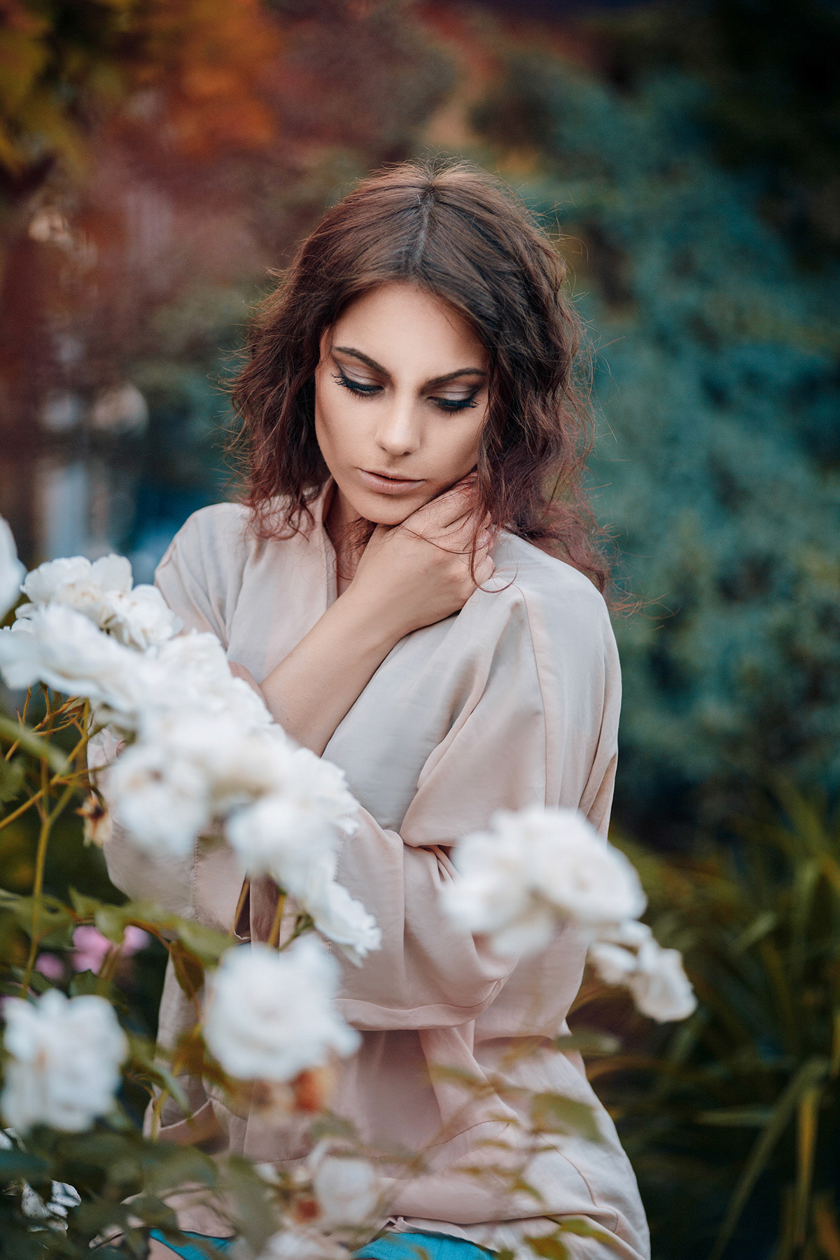 Beautiful young woman with curly hair near roses in a garden. Perfectly retouched.