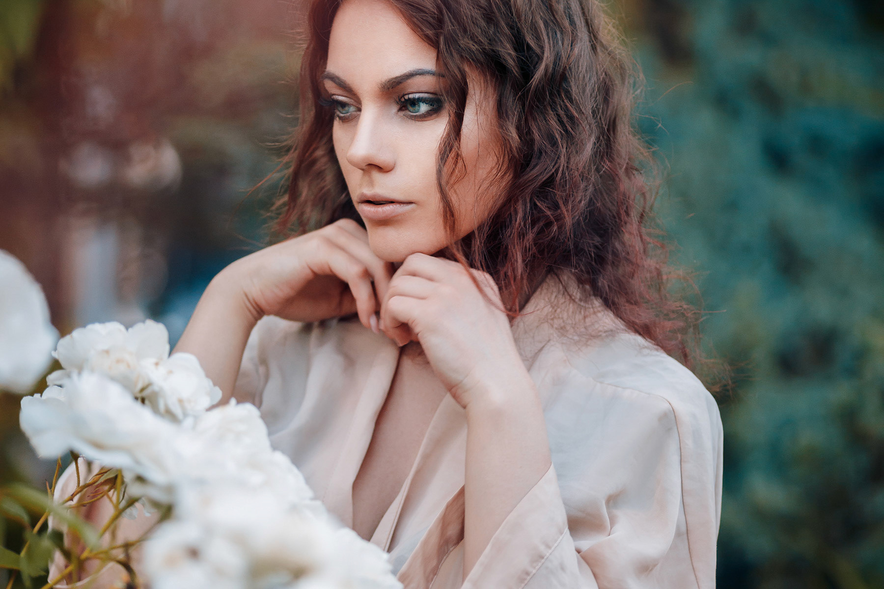 Beautiful young woman with curly hair near roses in a garden. Perfectly retouched.
