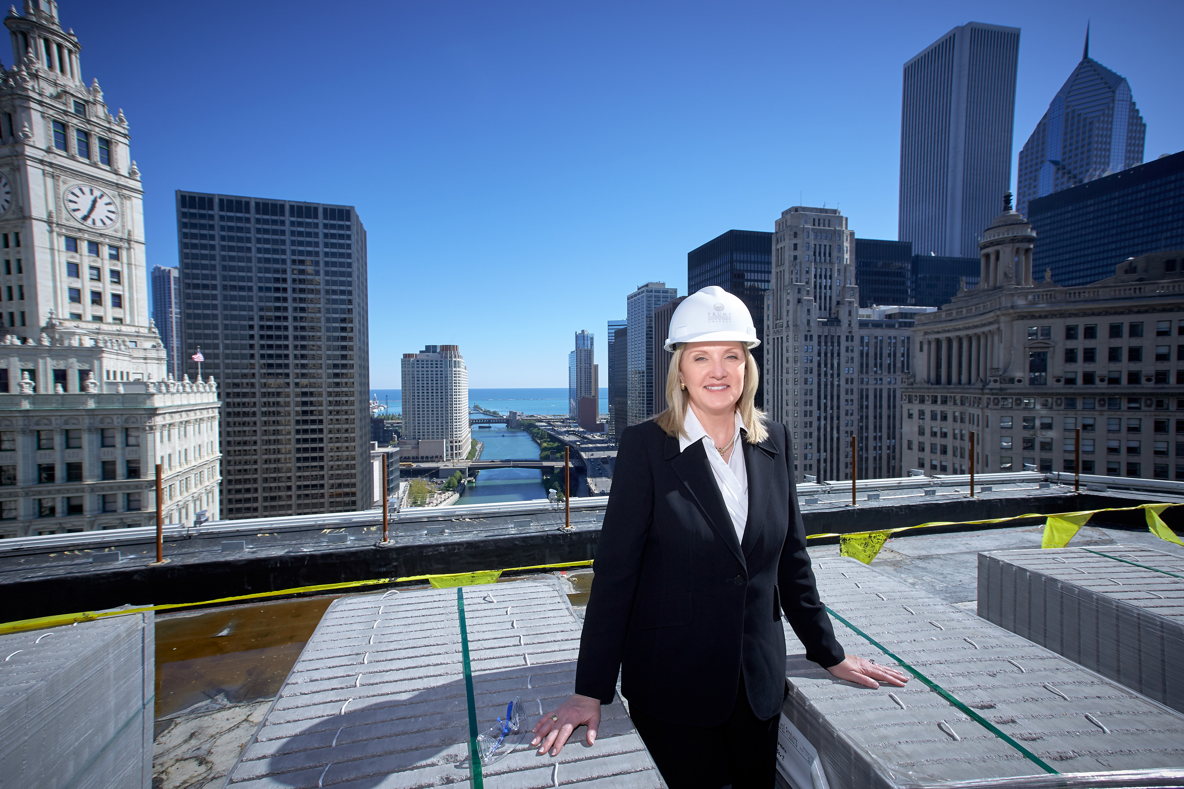 A woman realtor posing at Trump tower while under construction with the view of the Chicago River, Lake  Michigan, and city buildings in the background.