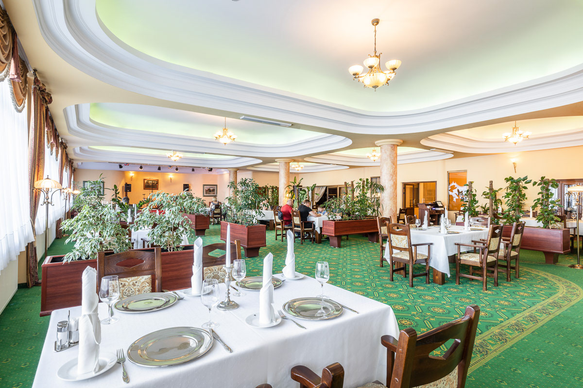 wnętrze restauracji hotelowej z zielonym dywanem i białymi nakryciami na stołach