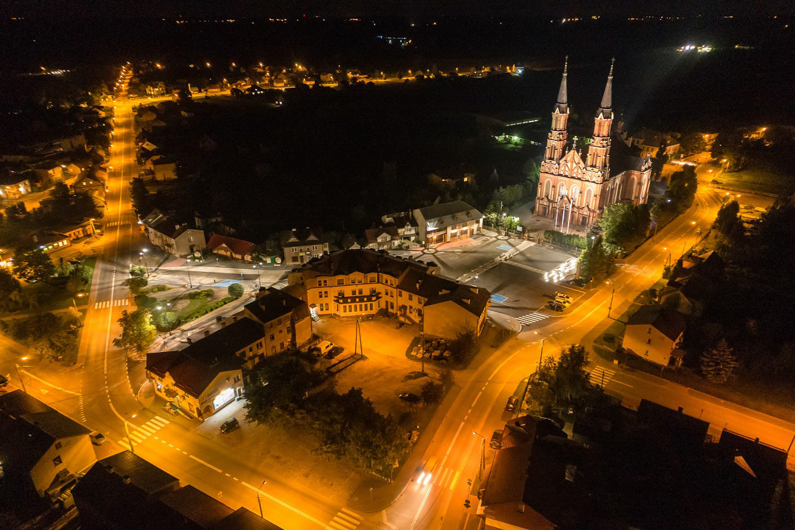 Ujęcie Katedry w Sokołach w aurze nocnej z autami na ulicach i Urzędem Gminy w dole