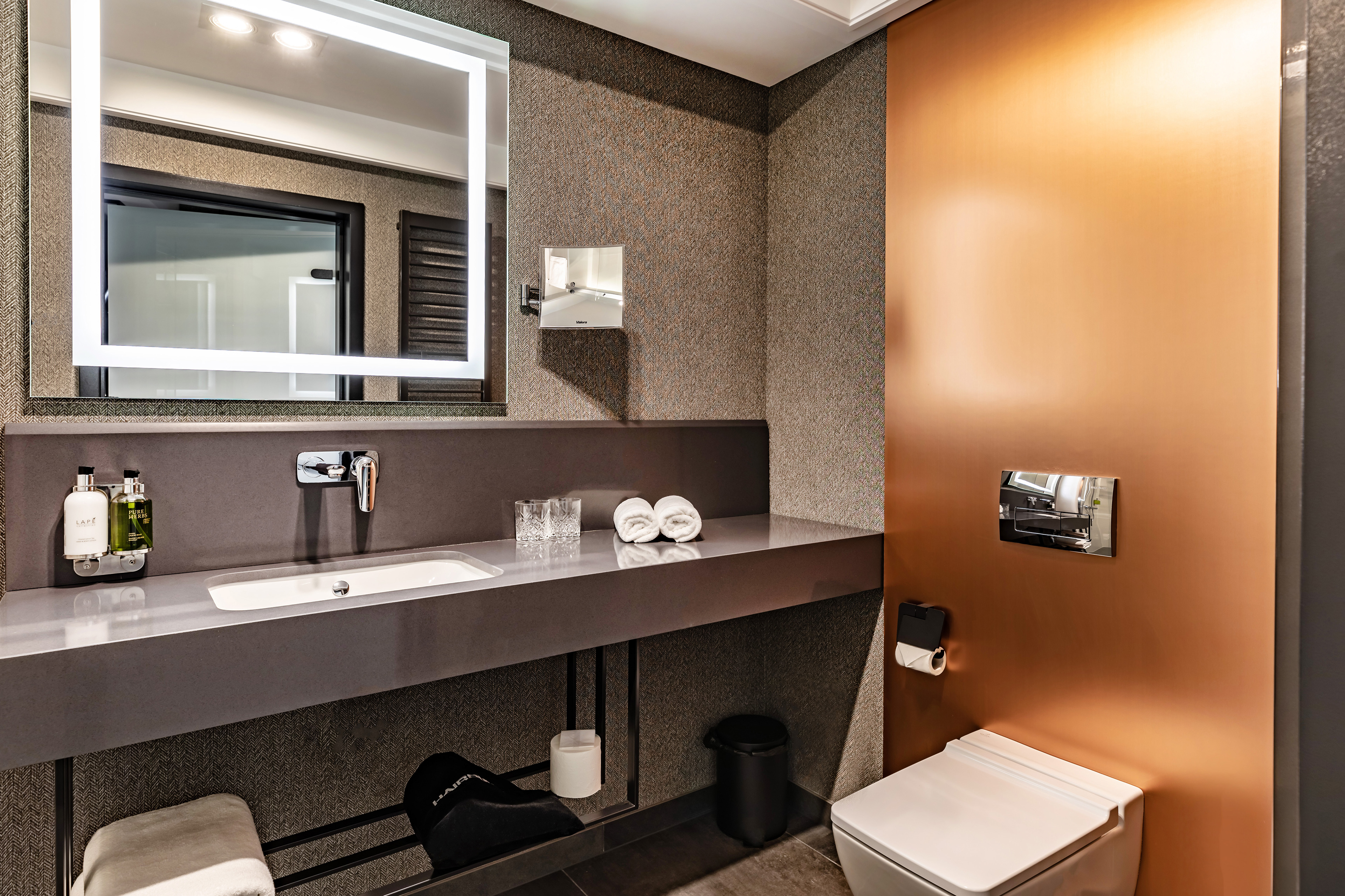 nowoczesna łazienka hotelowa z lustrem sedesem i pomarańczową miedzianą ścianą
