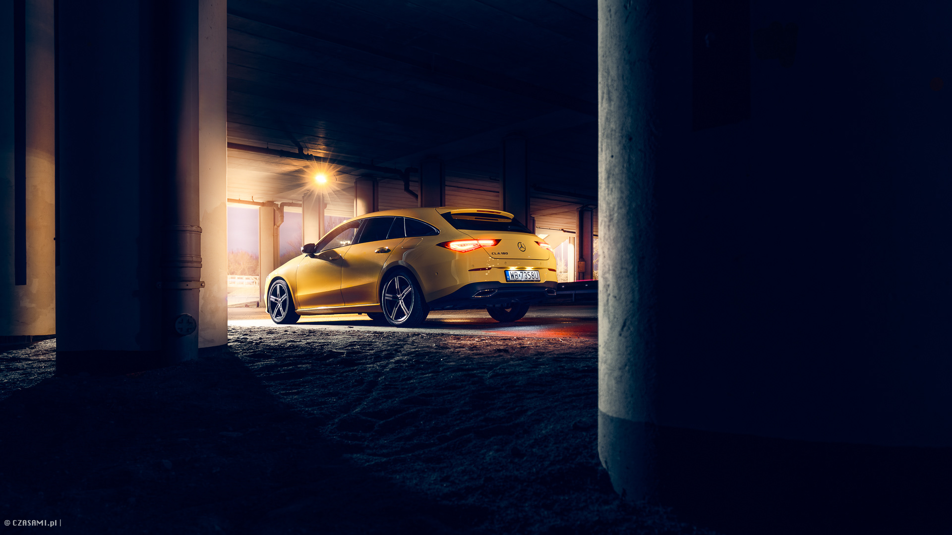 Mercedes Benz CLA 180 w pięknym żółtym kolorze, zaparkowany pod wiaduktem. Fotografia motoryzacyjna CZASAMI.pl