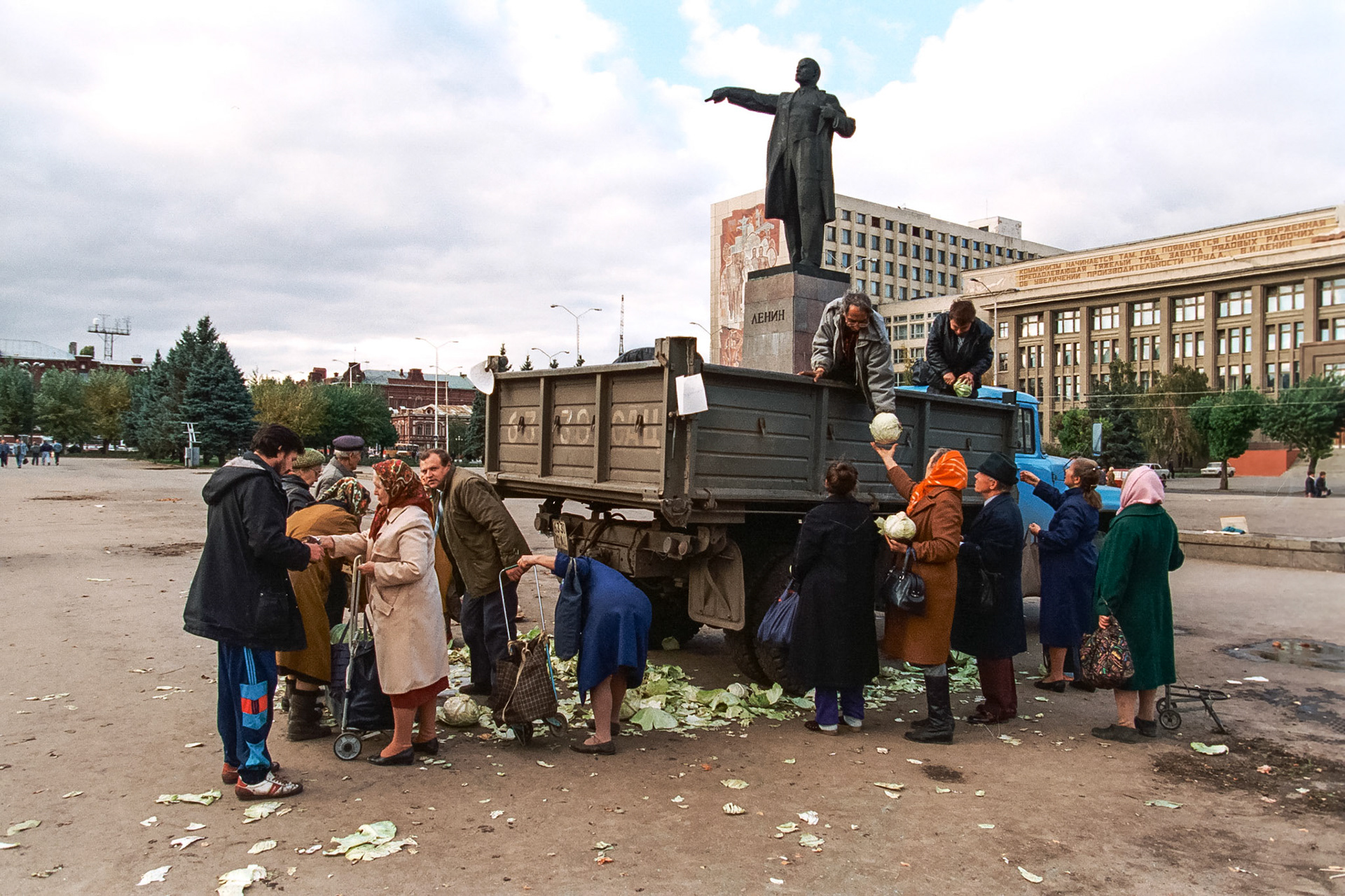 Under a statue of Lenin, a state-sponsored food truck unloads cabbage in a town square.