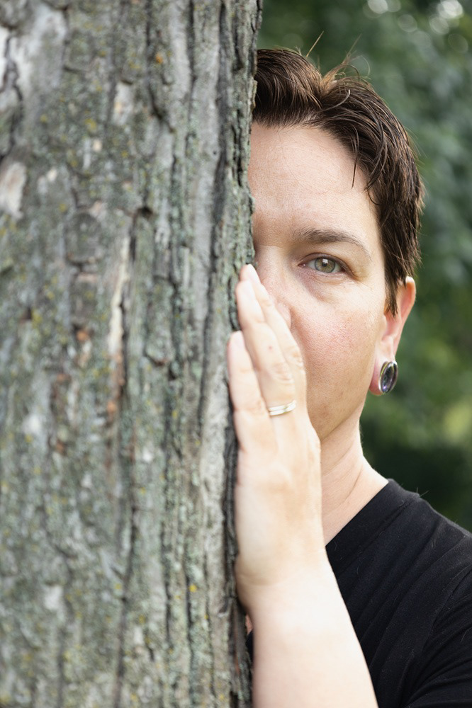 The photographer, Janine Benedict, peeking out from behind a tree