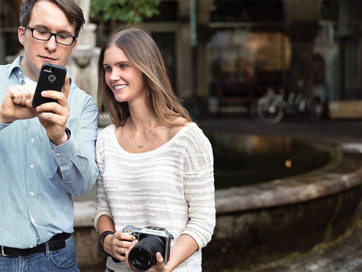 Chris Braun zeigt in der Praxis den Umgang mit Kameras vom iPhone bis zur Profikamera. Im Bild zu sehen ist Chris Braun mit einer Teilnehmerin mit Mittelformat Kamera, Chris Braun demonstriert auf seinem iPhone.