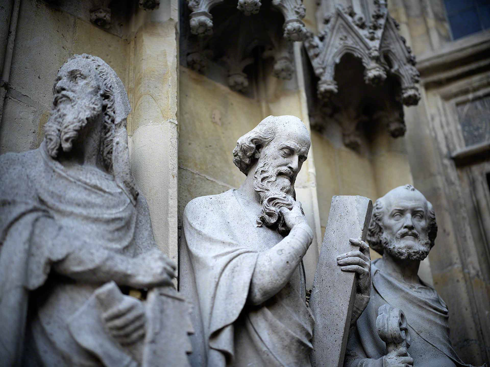 Bokehaufnahme dreier Steinfiguren am Westportal der Überwasserkirche in Münster, Westfalen. In der Mitte Simon Petrus durch sanftes Bokeh und stilvolle Vignettierung hervorgehoben.