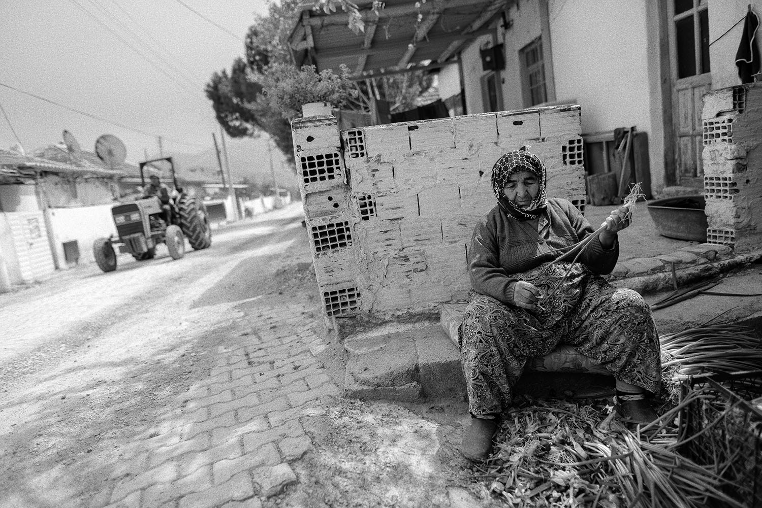 A woman sorting out onions with a tractor in the background in the village of Görece, Menemem in a black and white photo.