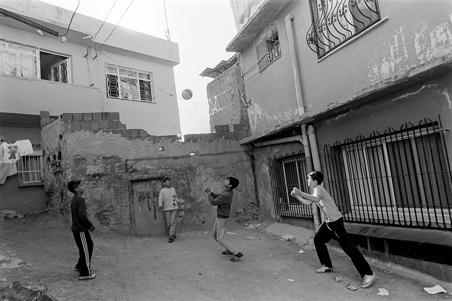 A group of children playing football around their house on the street, photographed on Kodak Trix 400 in Kadifekale District in İzmir, Türkiye.