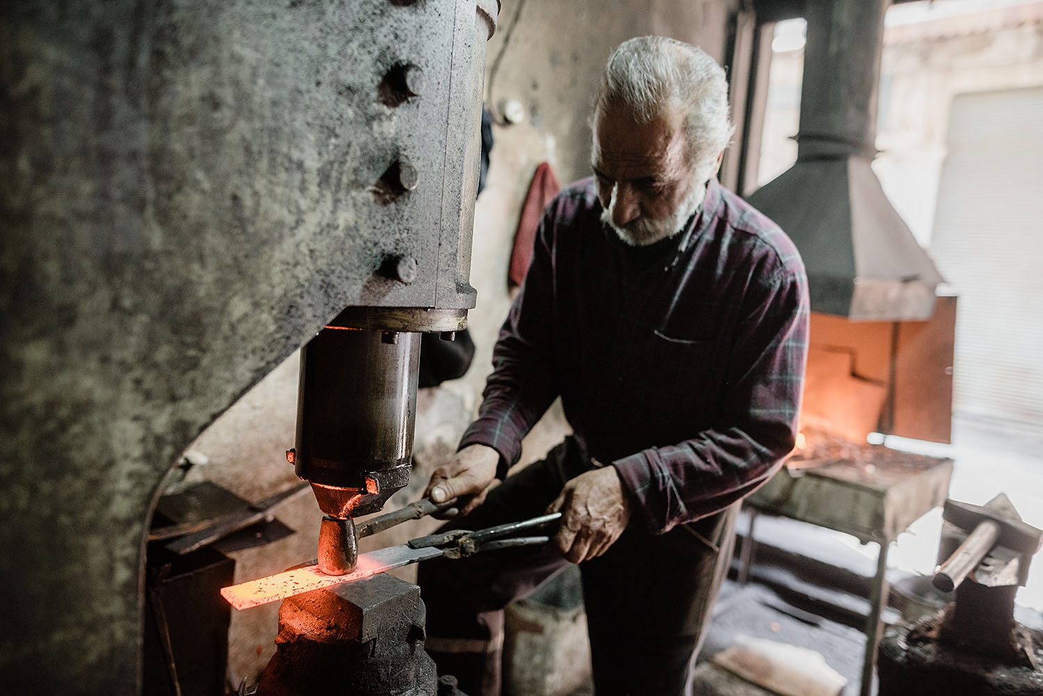 An ironsmith is working on a piece of iron and using tools to shape the metal.