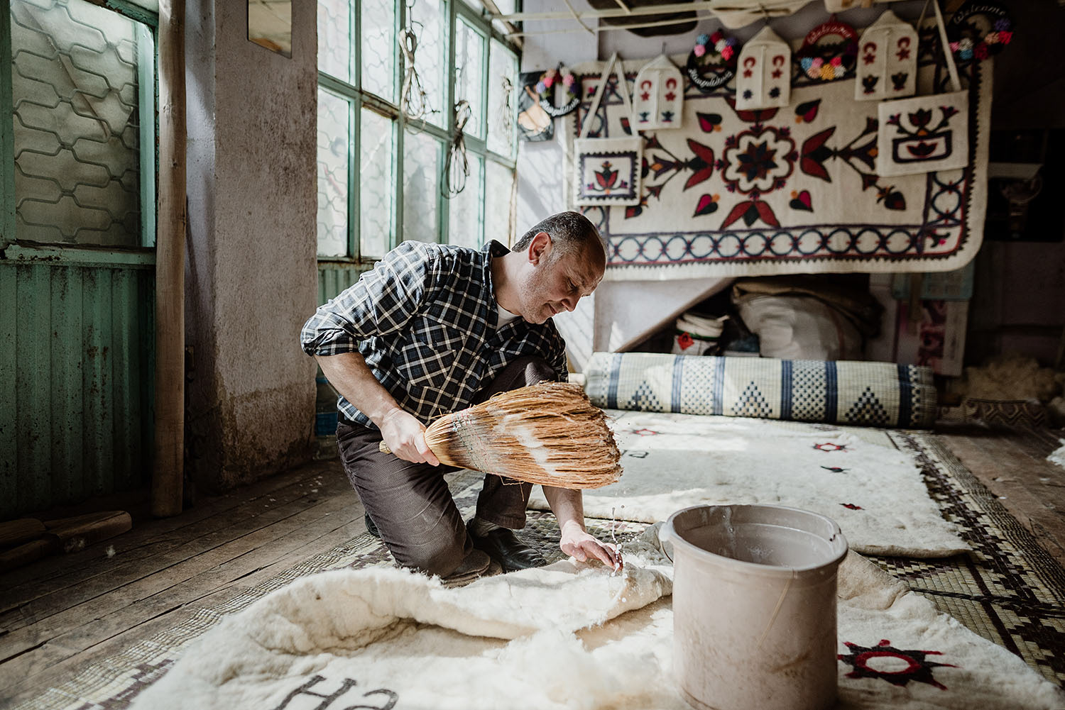 A traditional feltmaker is wetting and preparing the felt laid flat on the ground.