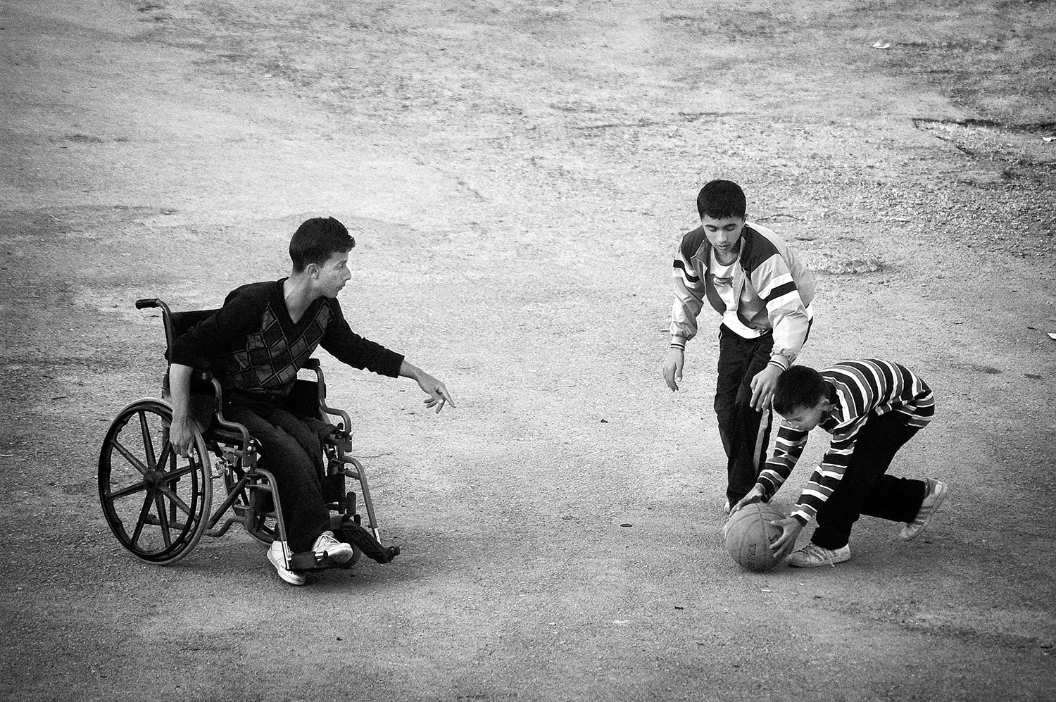 A disabled kid on a wheelchair playing basketball with two other kids.