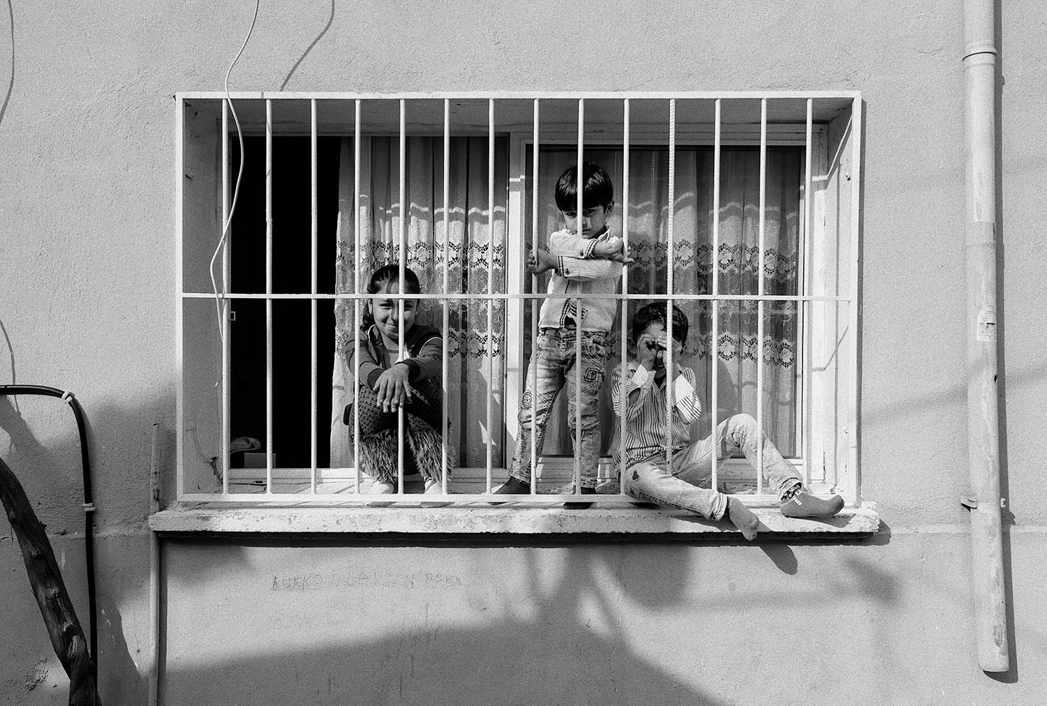 Children watching the street behind the window bars of their home.