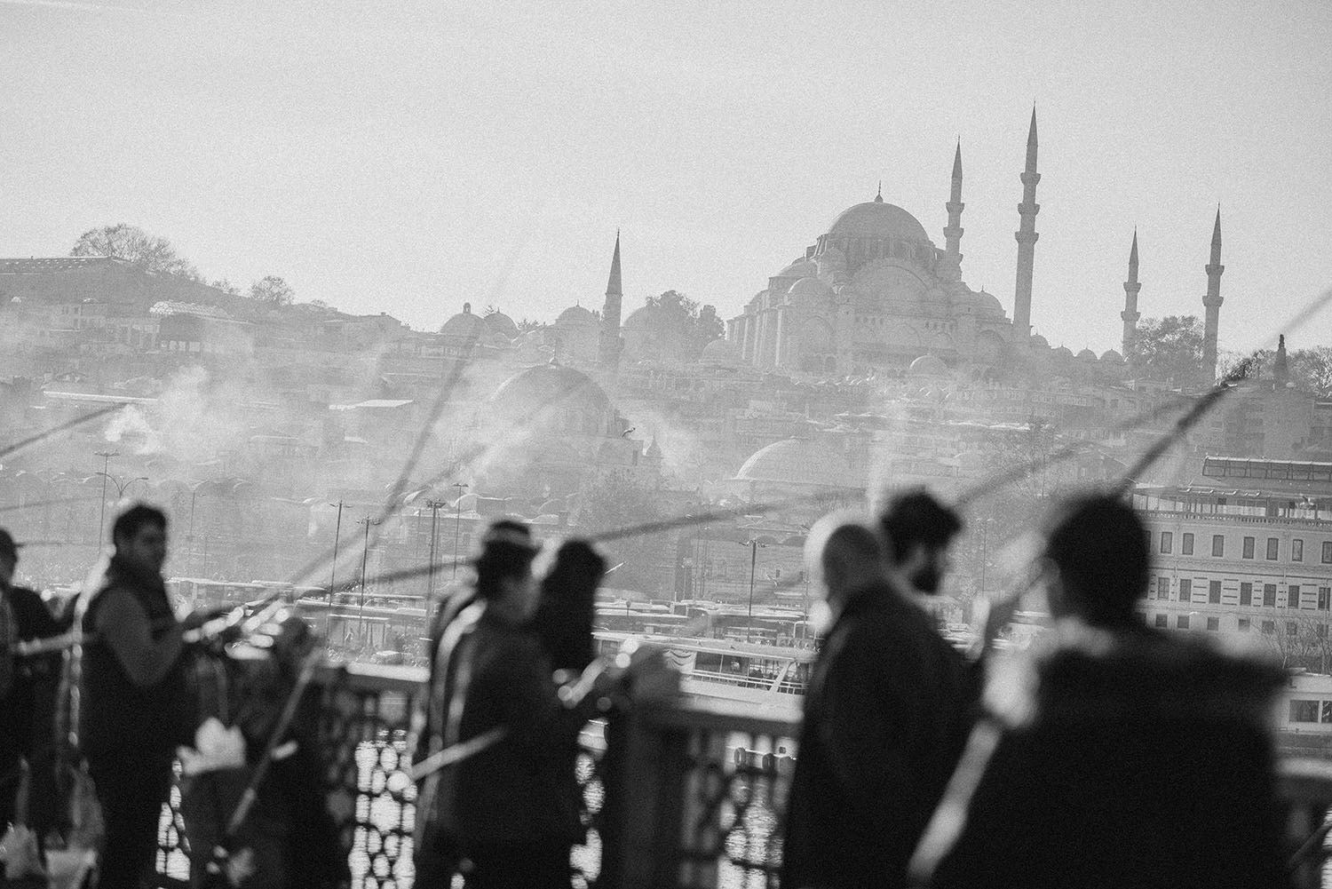 People fishing on Haliç Bridge with a mosque in the background.