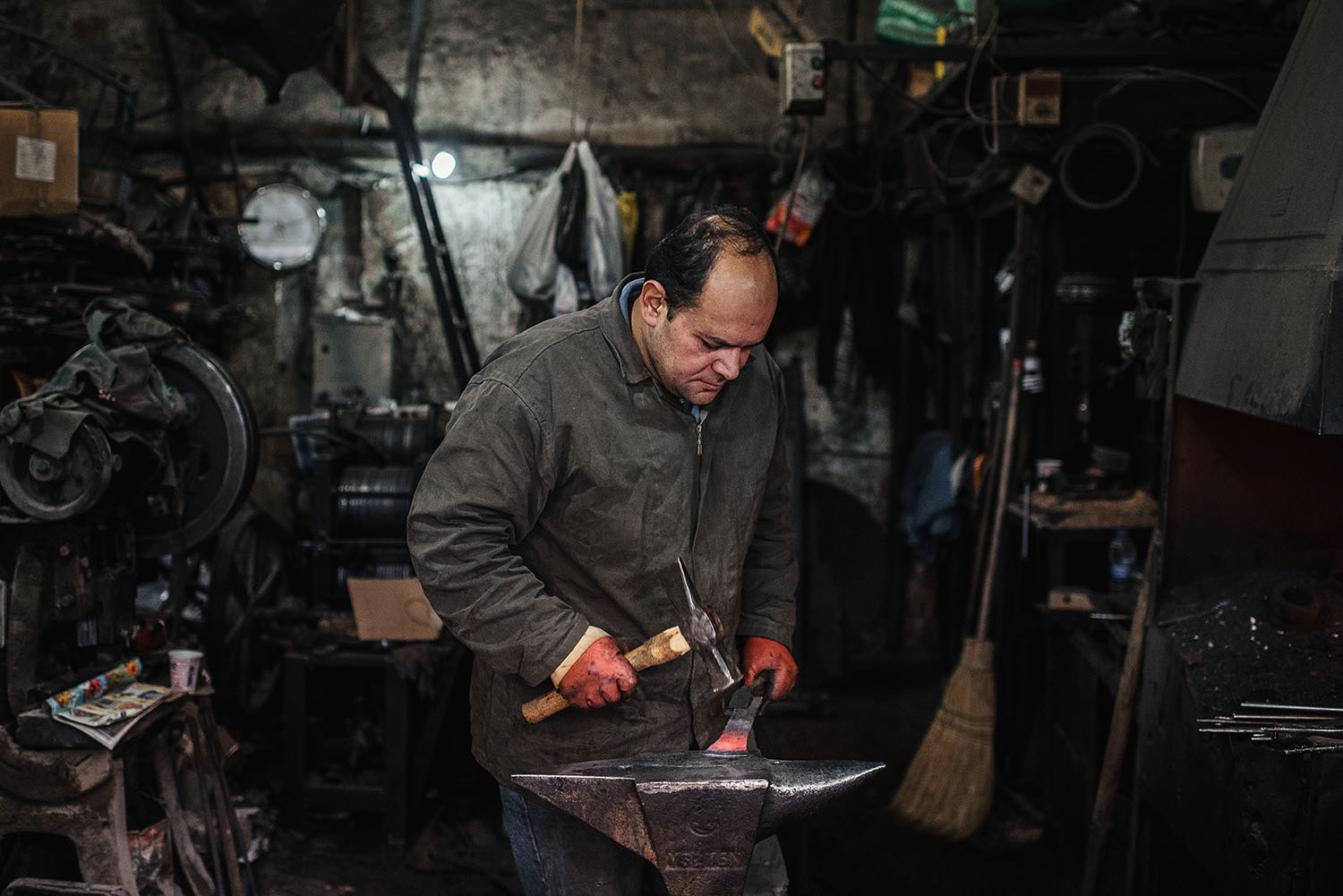 A tinsmith with a hammer working on shaping a piece of hot iron.