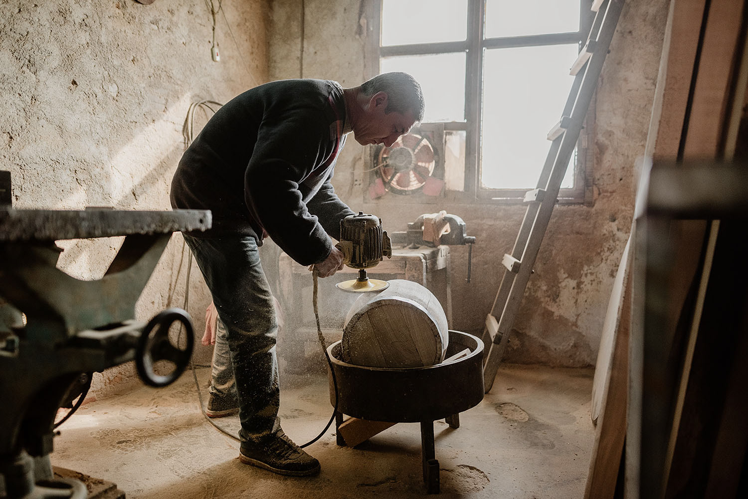 A barrel maker sanding the surface of a wooden barrel in his workshop.