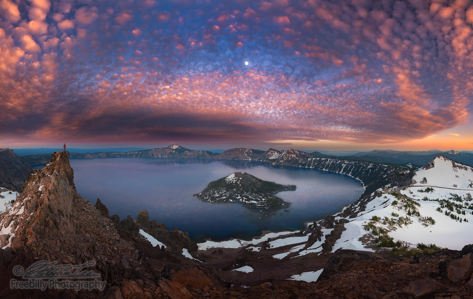 Man on hilltop viewing Crater Lake with full moon at dusk