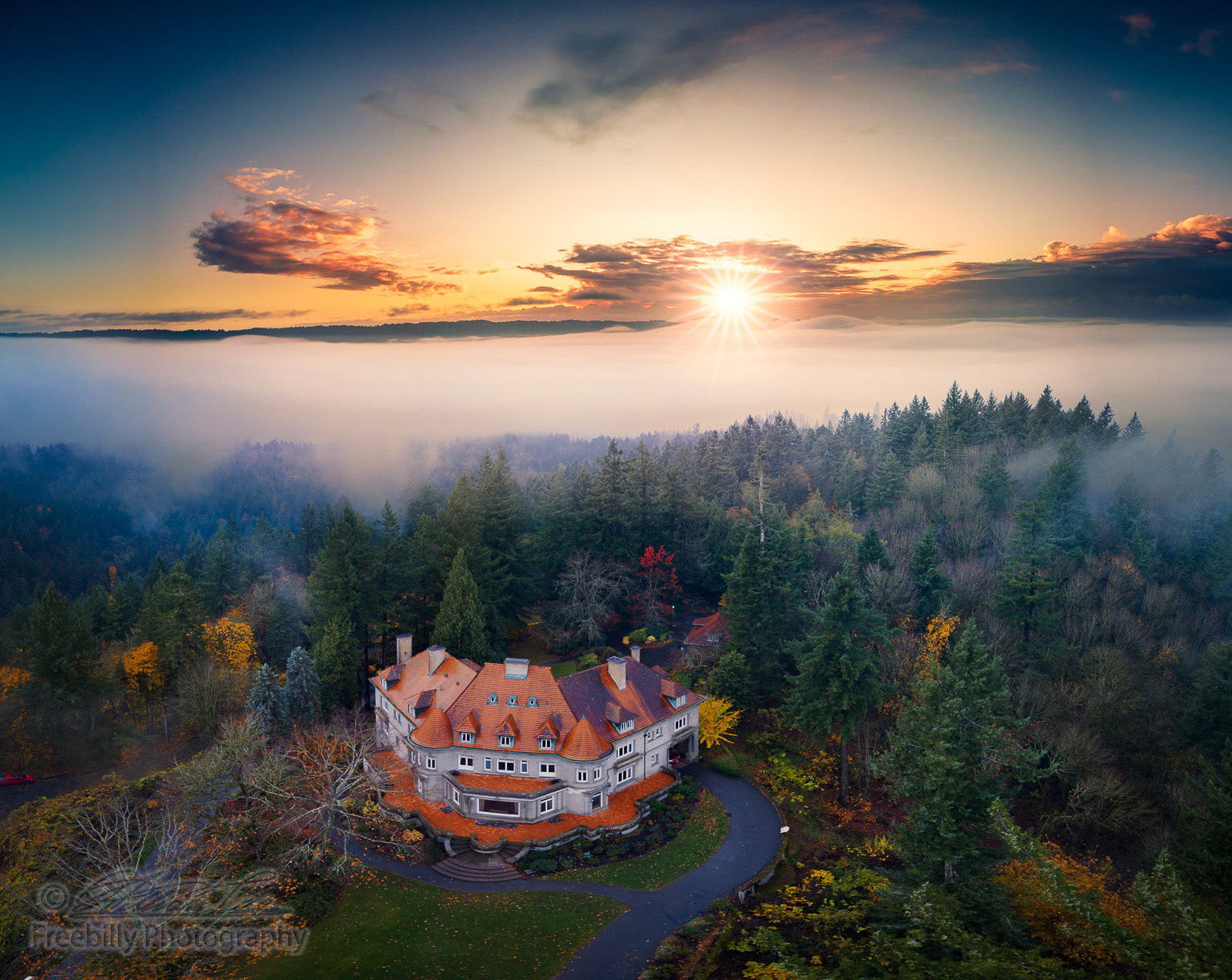 A fine art photo of a heritage mansion museum in forest with autumn foliage against rolling fog and shining sun