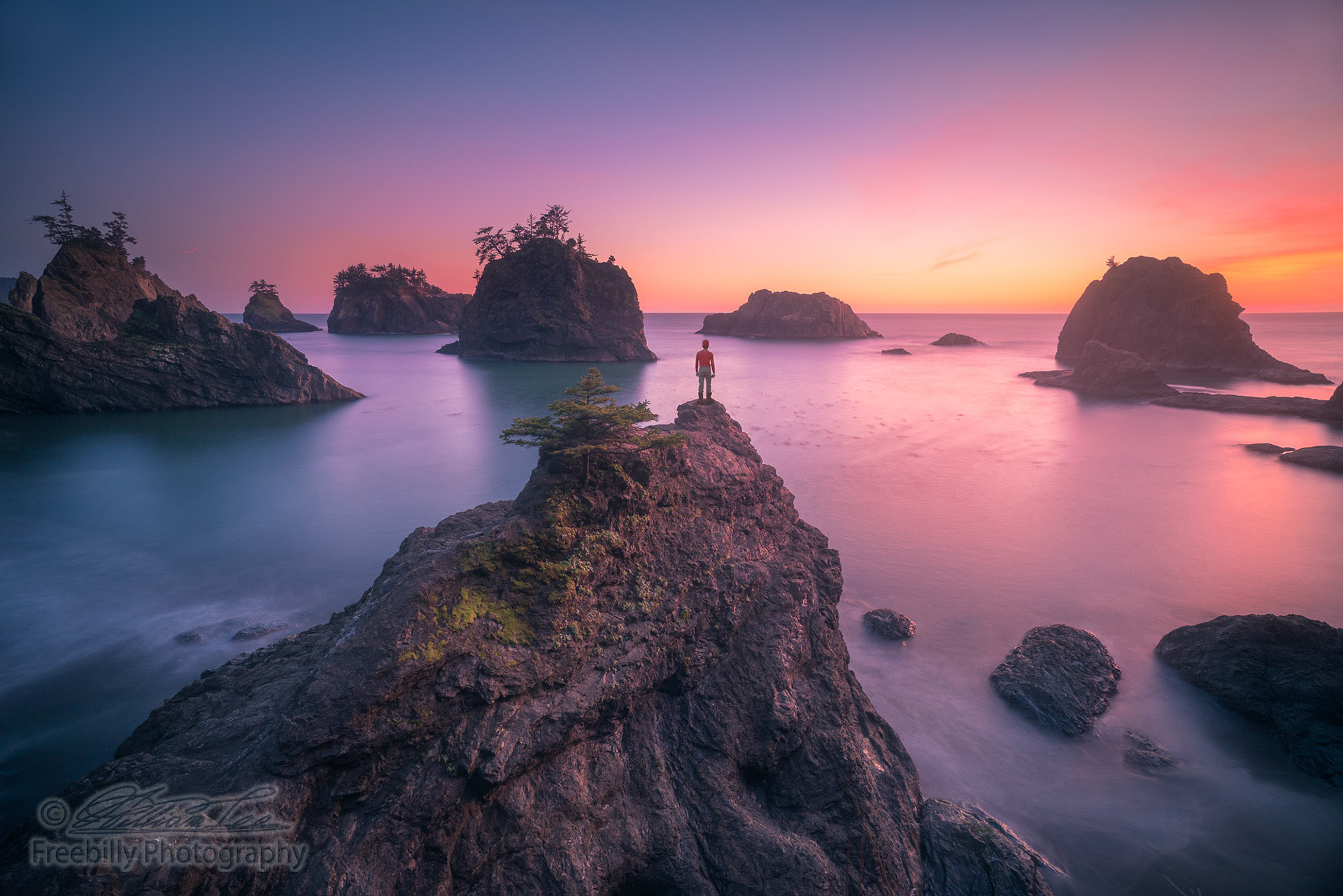This is a photograph of a man standing on top of seastack and watching sunset of Oregon coast.
