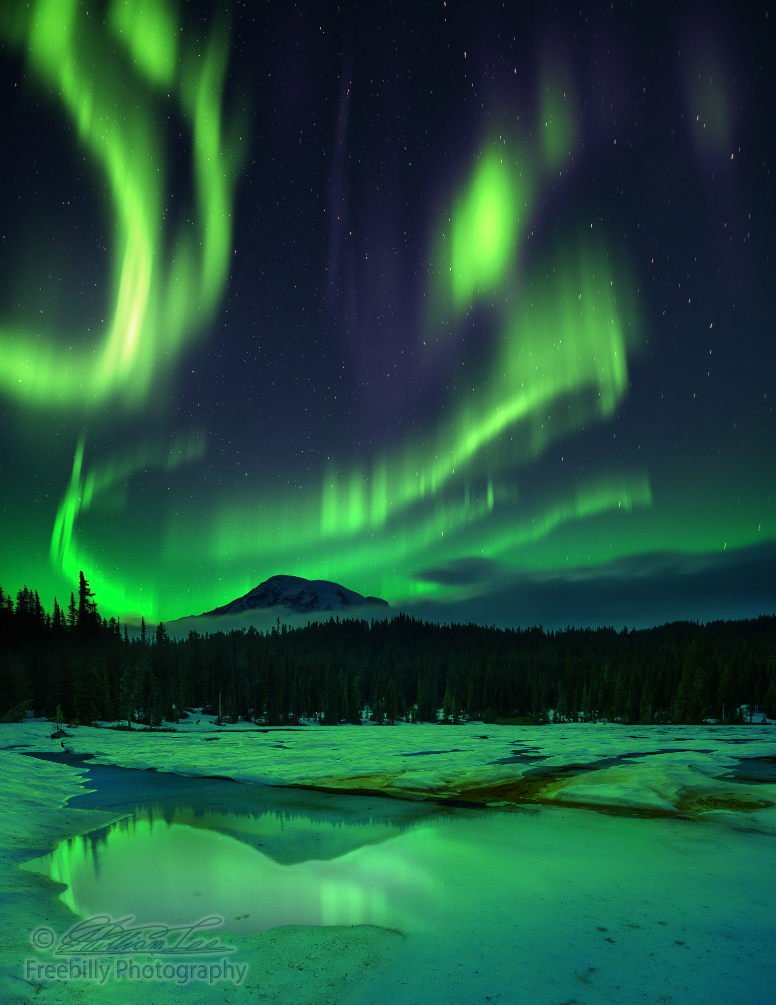 This is a photograph of night sky with aurora borealis and stars over frozen lake with reflections