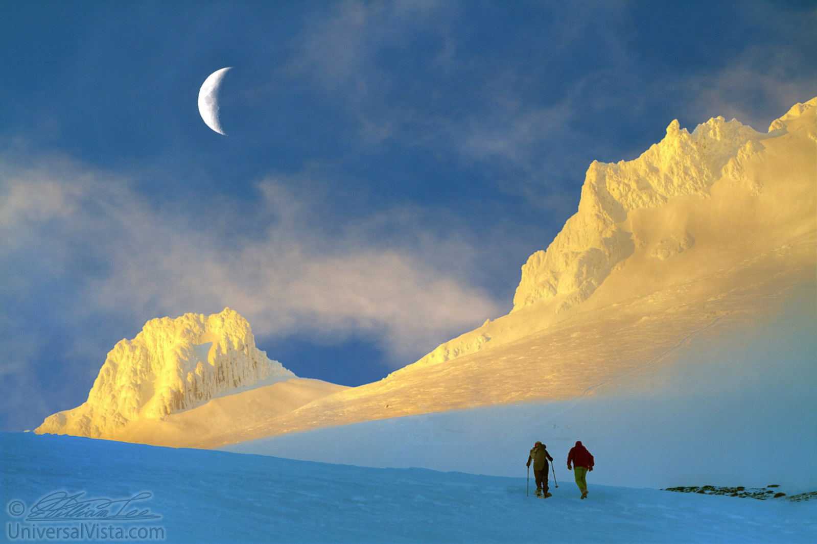 This is a photograph of a nature scene in Mt. Hood with two persons snowshoeing/hiking toward the peak. Photo was taken around sunset hour with moon and clouds.