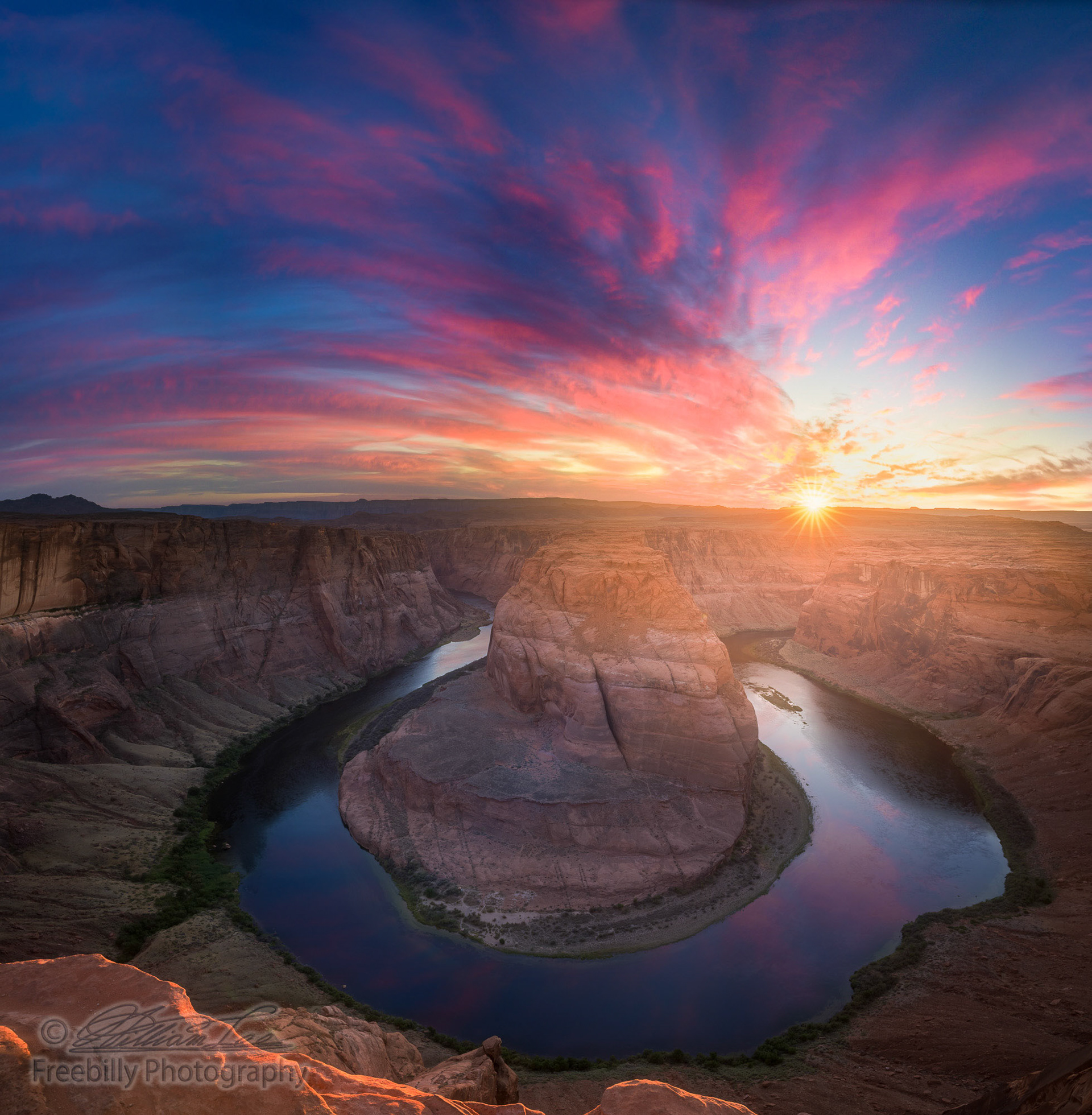 A super wide angle view of the beautiful Horseshoe Bend sunburst sunset and colorful clouds with reflections