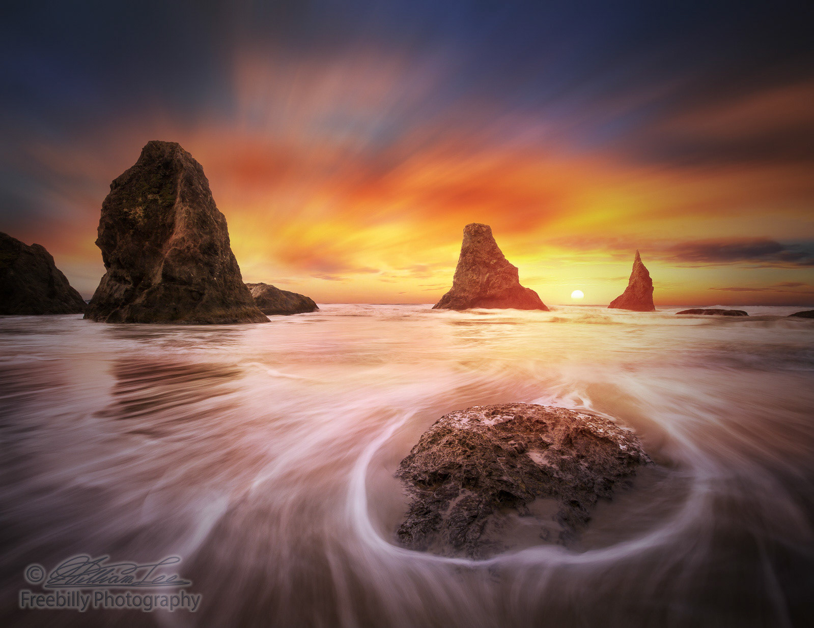 This is a seascape photo with stacks, ocean flux, setting sun and colorful clouds.