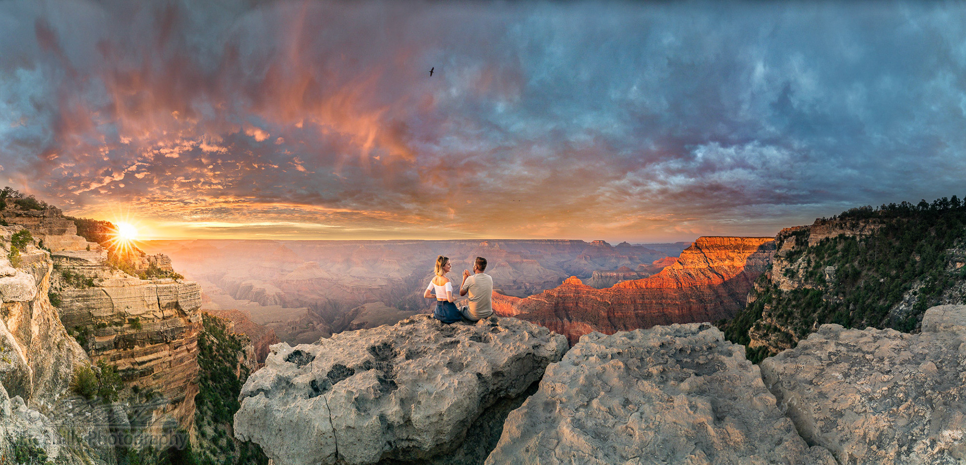 This is a panoramic photograph of a man and a woman sitting on the edge of rim, talking about future and watching the Grand Canyon sunset while bird in the sky
