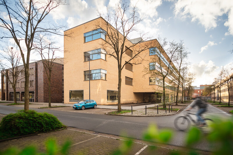 Architekturfoto des BIOM Gebäudes an der Bremer Uni. Gelber Backstein. Ein unscharfer Radfahrer im Vordergrund.. Architektur: kister scheithauer gross