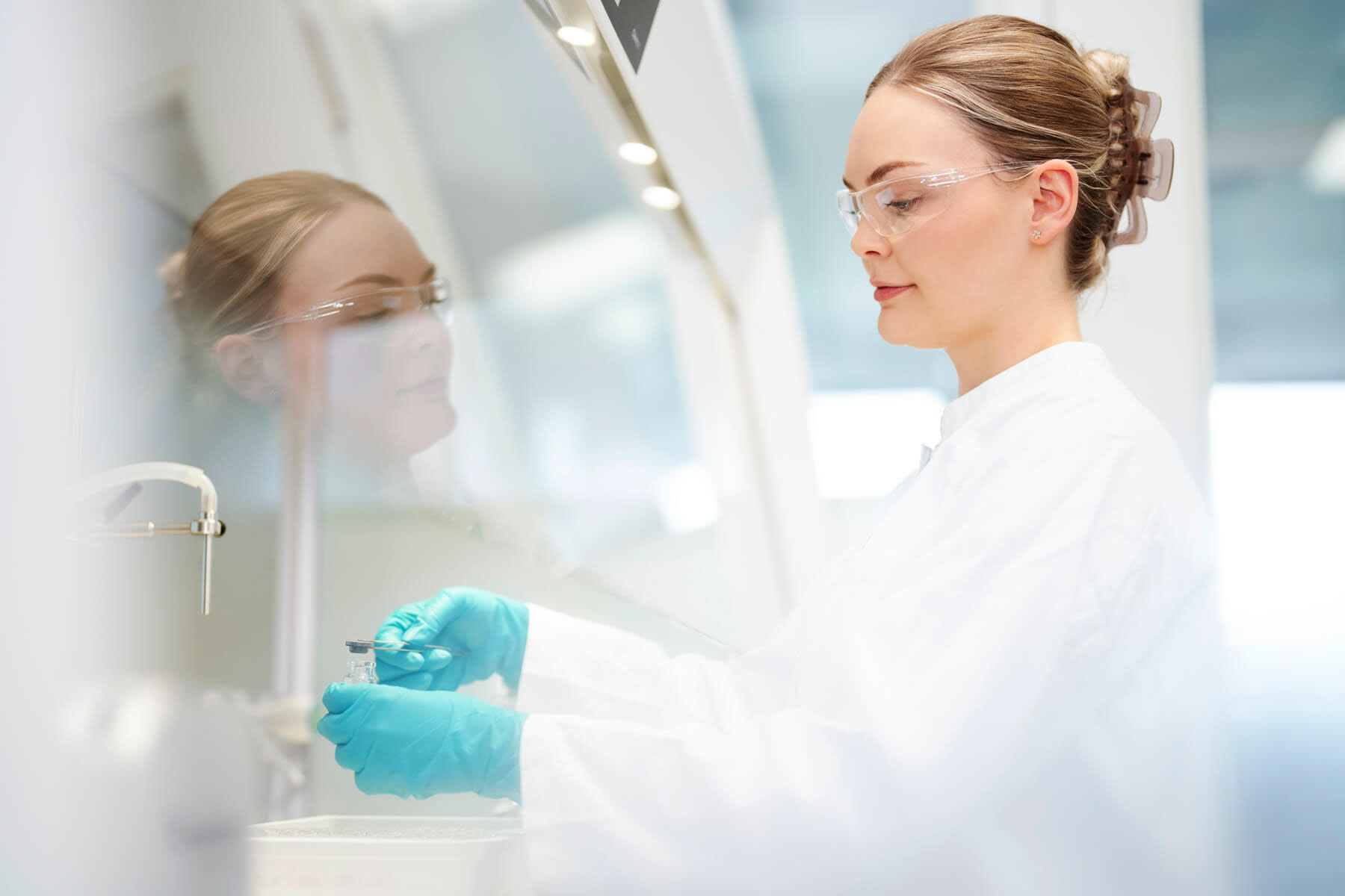 Ästhetisches Foto einer Labormitarbeiterin an einem Arbeitsgerät mit Spiegelung und Unschärfe.