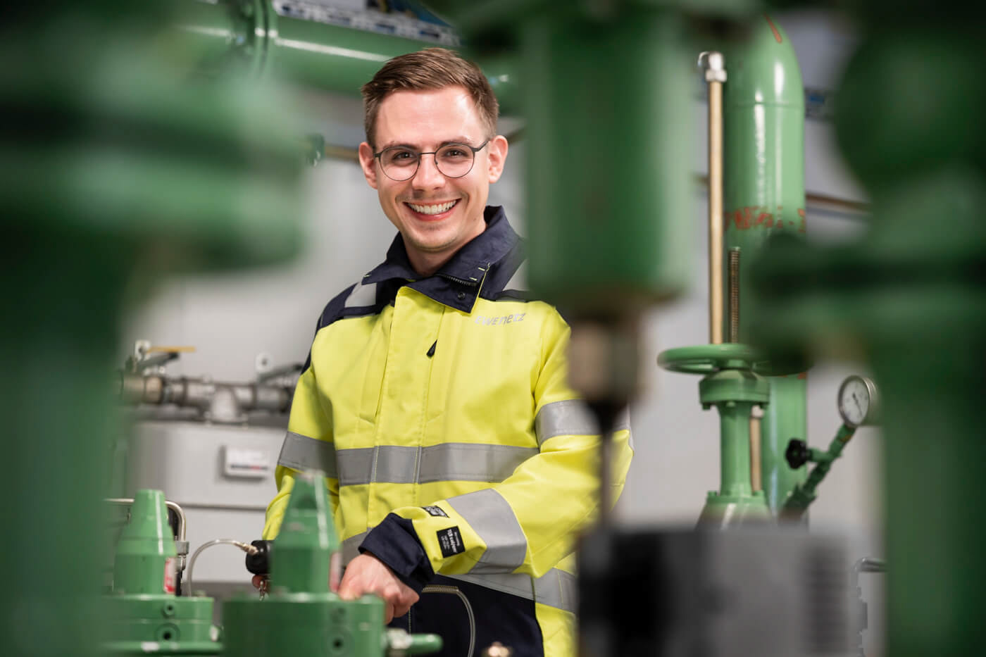 Junger Mitarbeiter des Netzbetreibers EWE Netz schaut in einer Gasregelanlage lächelnd in die Kamera.