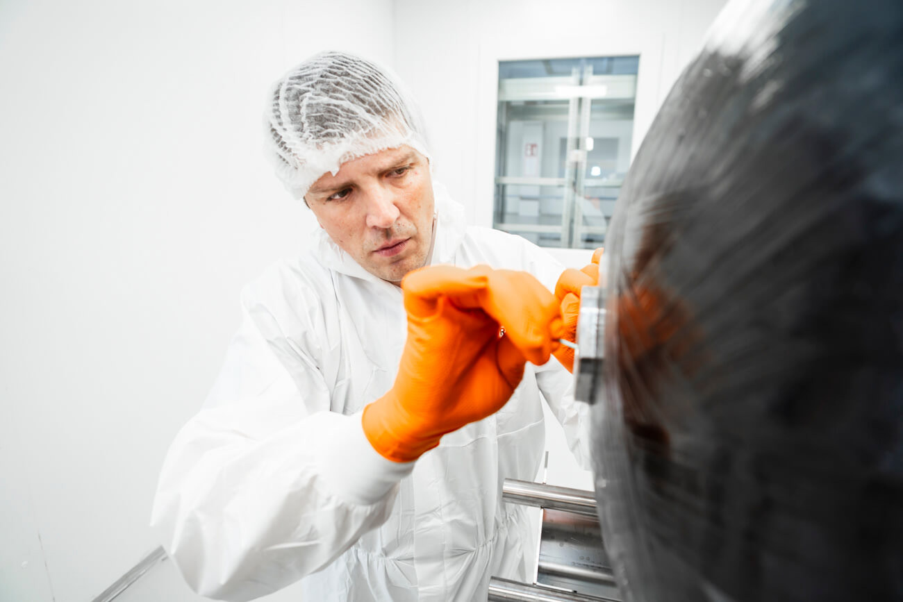 Mitarbeiter in Schutzkleidung bearbeitet einen Wasserstofftank. Industriefotografie für Hykonis.