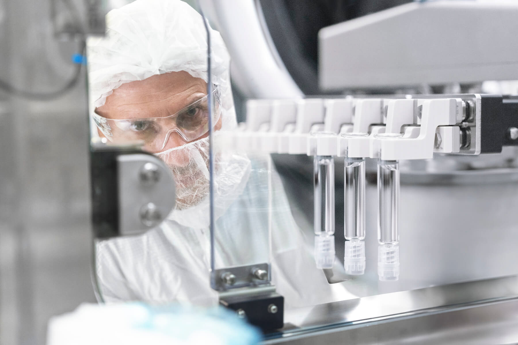 Mitarbeiter mit PSA bei Fotoshooting in der Pharmabranche schaut in einen Isolator.