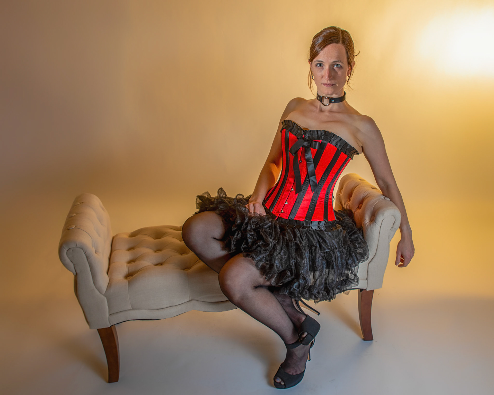 Western Corsetry - Fainting on the Fainting Couch: Bringing back out the western themed corset outfit for a final run at studio shots with the seamless backdrop. Godox v1 with 7" reflector front left, 30x120 softbox with another Godox V1 right side, and Godox AD200 w/ Yellow gel lighting the backdrop.
