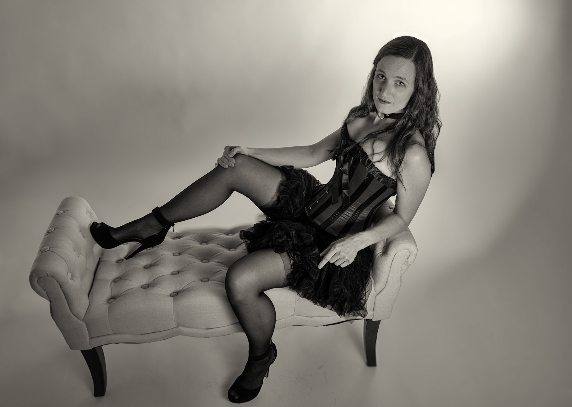 Western Corsetry - Reclining on the Fainting Couch (B&amp;W): Bringing back out the western themed corset outfit for a final run at studio shots with the seamless backdrop. Godox v1 with 7" reflector front left, 30x120 softbox with another Godox V1 right side, and Godox AD200 w/ Yellow gel lighting the backdrop.