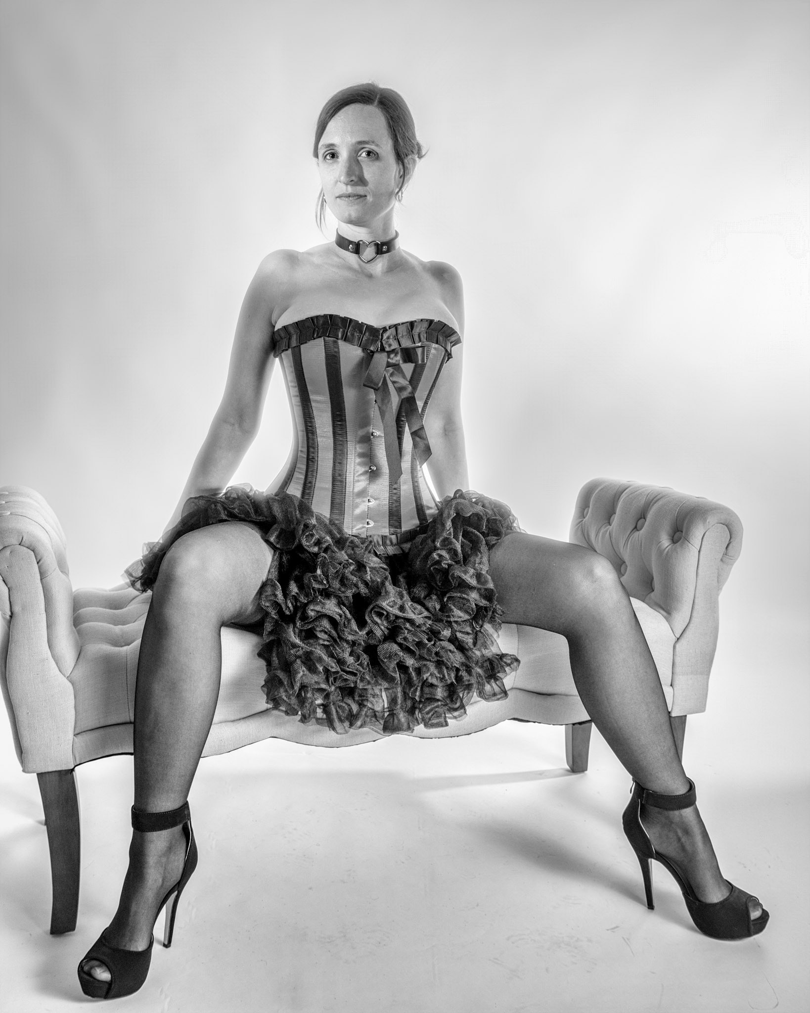 Western Corsetry - Posing on the Fainting Couch: Bringing back out the western themed corset outfit for a final run at studio shots with the seamless backdrop. Godox v1 with 7" reflector front left, 30x120 softbox with another Godox V1 right side, and Godox AD200 w/ Yellow gel lighting the backdrop.