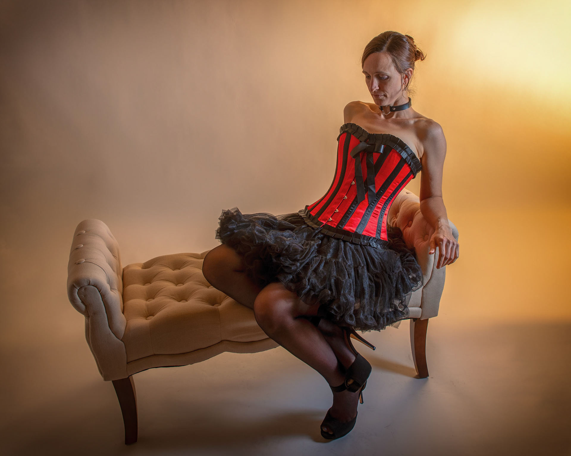Western Corsetry - Reclined: Bringing back out the western themed corset outfit for a final run at studio shots with the seamless backdrop. Godox v1 with 7" reflector front left, 30x120 softbox with another Godox V1 right side, and Godox AD200 w/ Yellow gel lighting the backdrop.