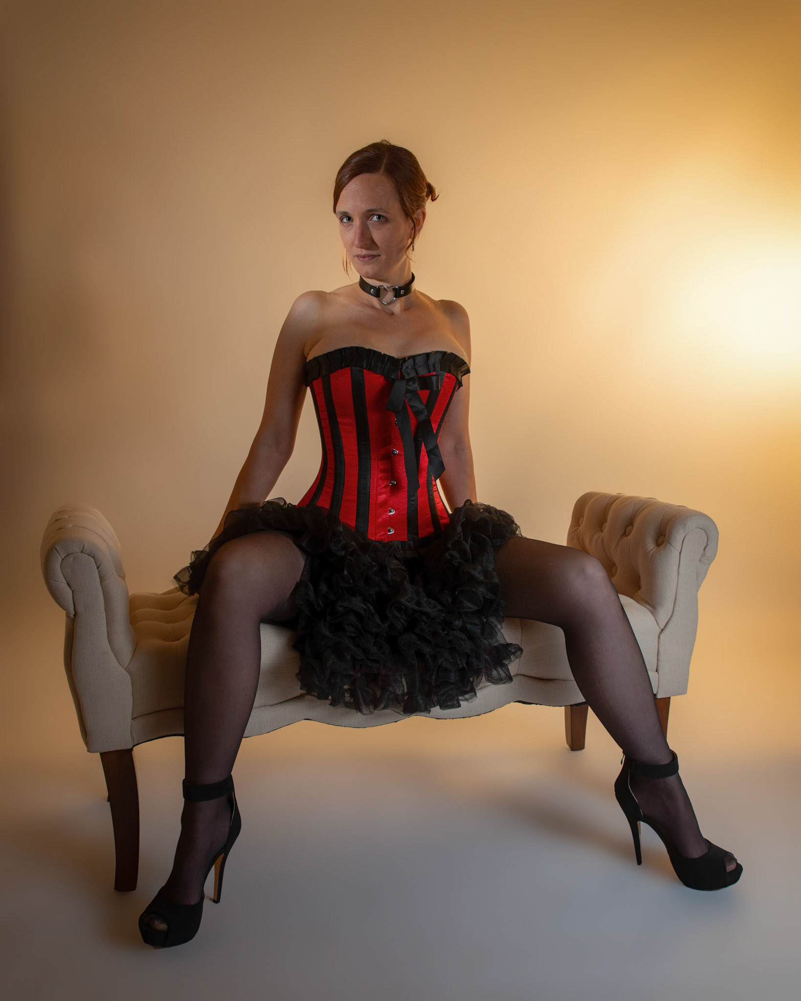 Western Corsetry - Posing on the Fainting Couch: Bringing back out the western themed corset outfit for a final run at studio shots with the seamless backdrop. Godox v1 with 7" reflector front left, 30x120 softbox with another Godox V1 right side, and Godox AD200 w/ Yellow gel lighting the backdrop.