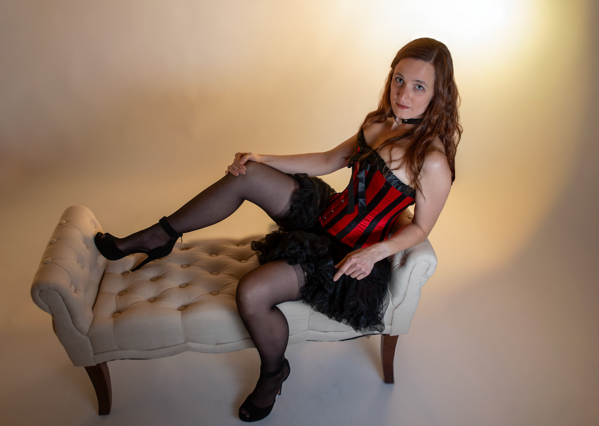 Western Corsetry - Reclining on the Fainting Couch: Bringing back out the western themed corset outfit for a final run at studio shots with the seamless backdrop. Godox v1 with 7" reflector front left, 30x120 softbox with another Godox V1 right side, and Godox AD200 w/ Yellow gel lighting the backdrop.
